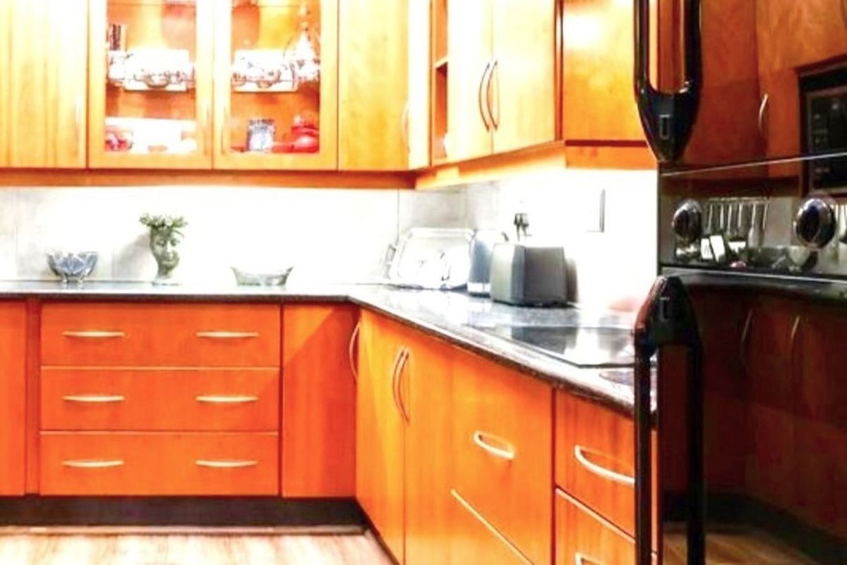 A functional kitchen featuring warm-toned wooden cabinetry, dark stone countertops, and integrated black appliances, providing ample storage and workspace.