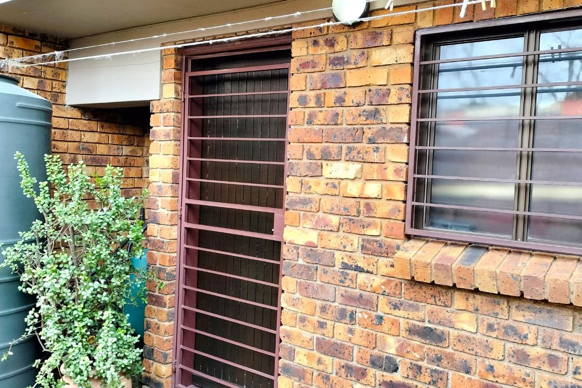 Exterior view of a brick facade featuring a security gate, window with security bars, and a large water storage tank.