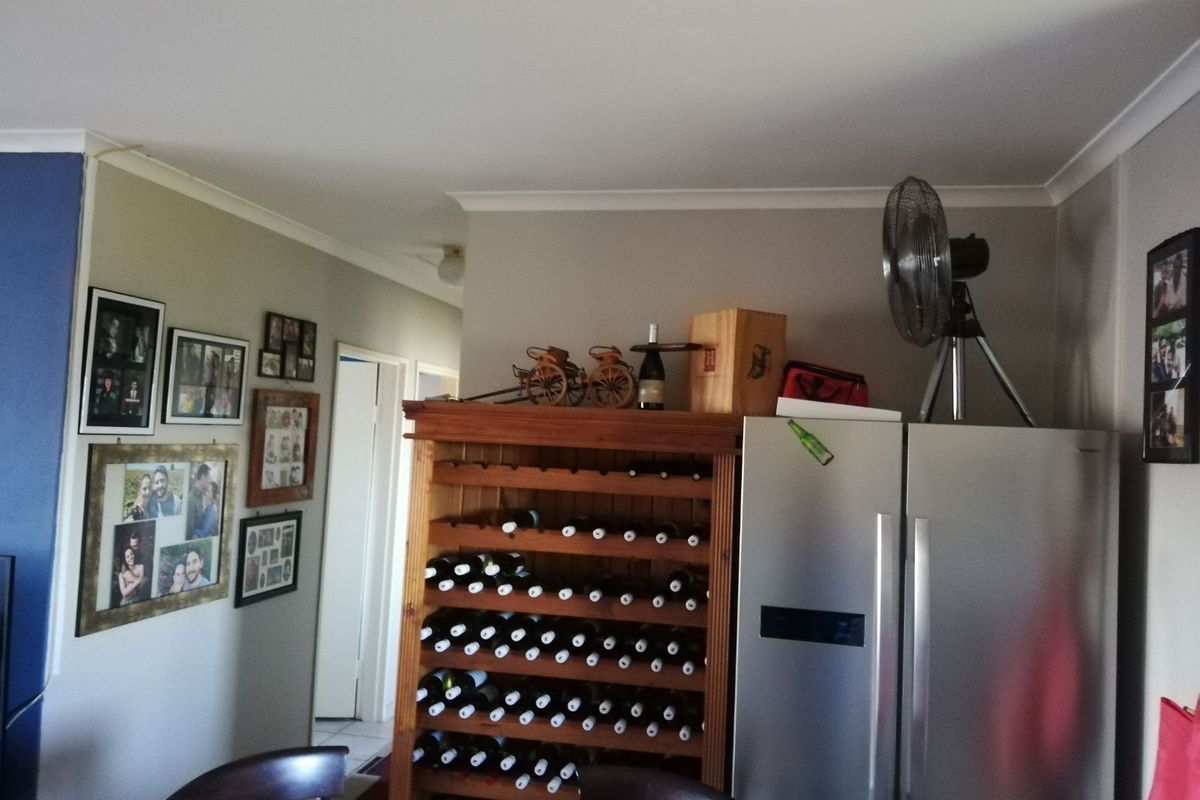 A view of a living area featuring a built-in wooden wine rack and space for a large refrigerator, with access to a hallway.