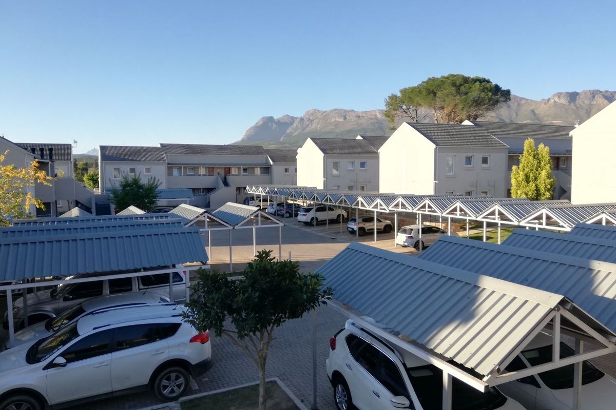 An elevated view of the apartment complex parking area featuring multiple covered carports and paved driveways against a mountain backdrop.