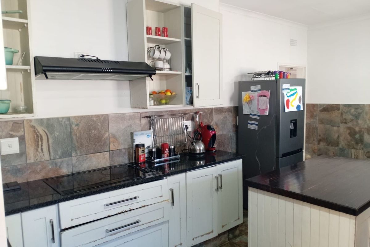 A kitchen featuring dark granite countertops, stone tile backsplash, built-in extractor fan, and white cabinetry with visible signs of wear.