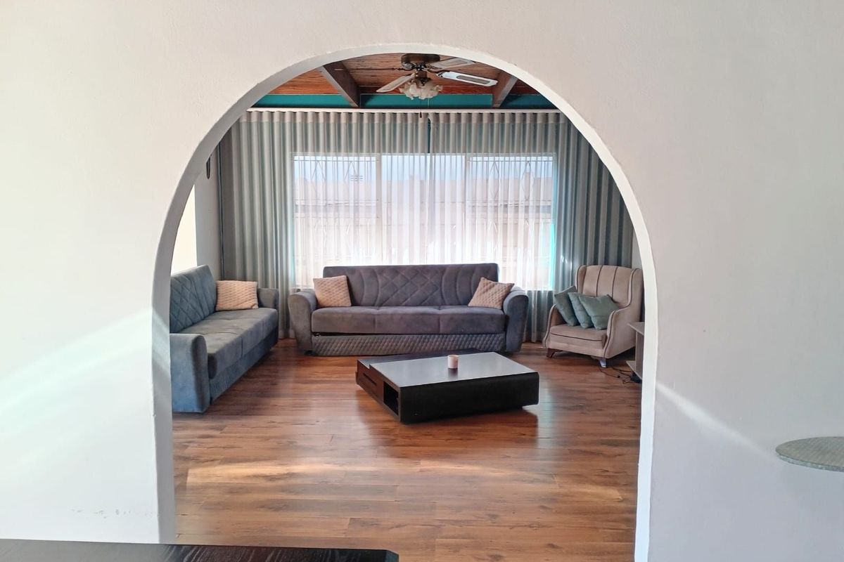 A cozy living room featuring a distinctive arched entryway, wood-look flooring, and a timber-beamed ceiling, creating a warm and inviting atmosphere.