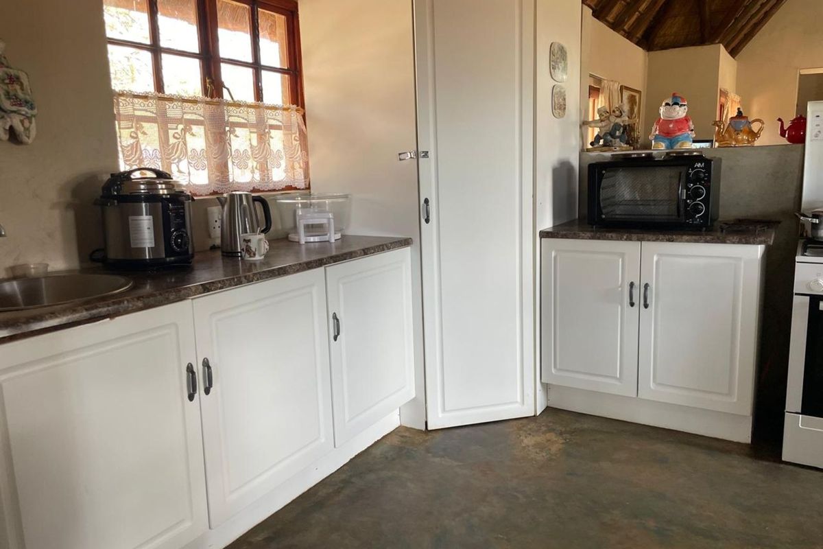 A rustic kitchen featuring white cabinetry, laminate countertops, a stainless steel sink, and a traditional thatched roof ceiling.
