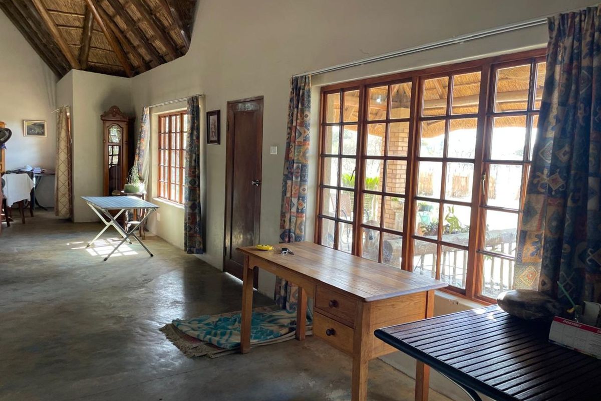 Spacious living area featuring a high vaulted thatched ceiling, exposed timber beams, and large wooden-framed windows providing natural light and garden access.