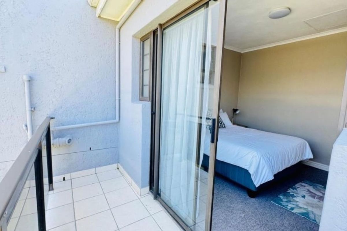 A bedroom with direct access to a private balcony through sliding glass doors, featuring neutral wall tones and carpeted flooring.
