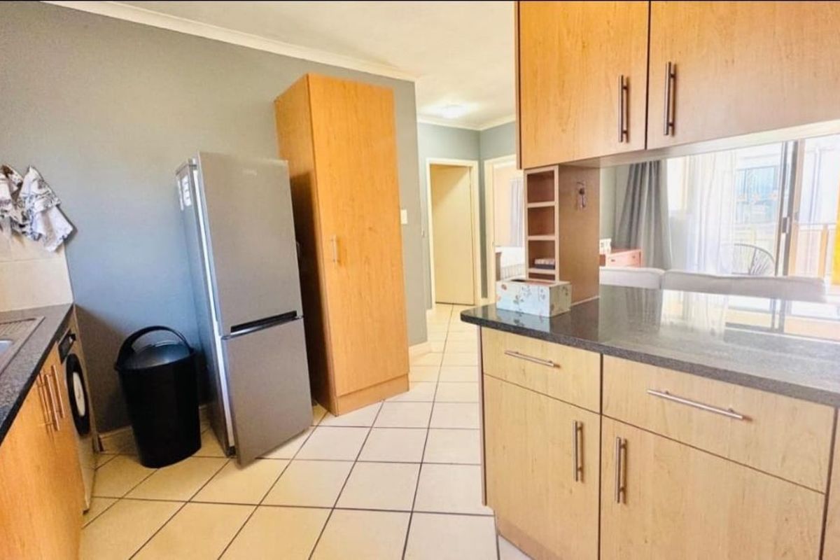 A functional kitchen area featuring light wood cabinetry, dark granite countertops, and tiled flooring, with an open-plan layout leading to the living space.