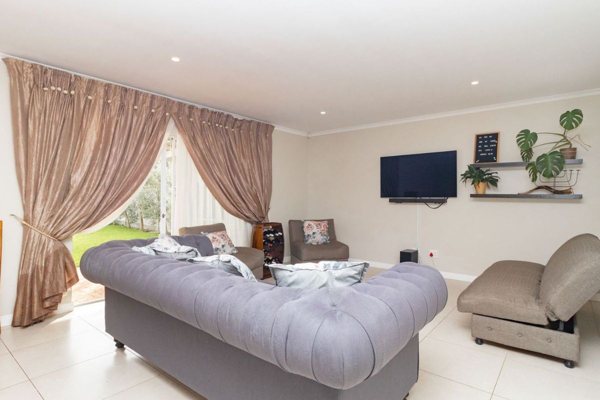 A bright and spacious living room featuring tiled flooring, recessed downlighting, and large sliding glass doors providing direct access to the garden.