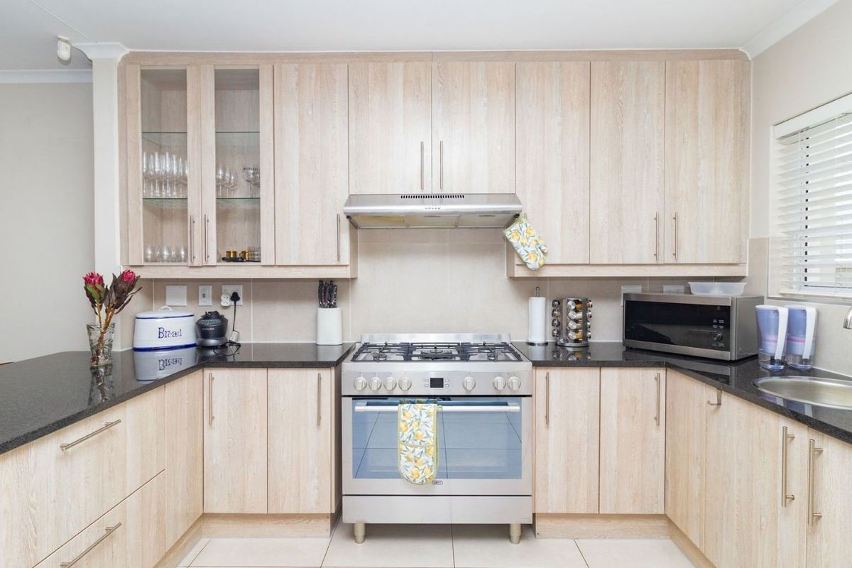 A well-maintained kitchen featuring light wood-grain cabinetry, dark granite countertops, a stainless steel gas stove with extractor fan, and a built-in sink.
