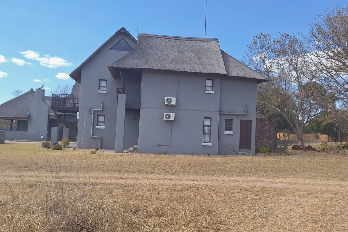 A rear view of a multi-story house featuring a traditional thatched roof, grey exterior walls, and mounted air conditioning units.