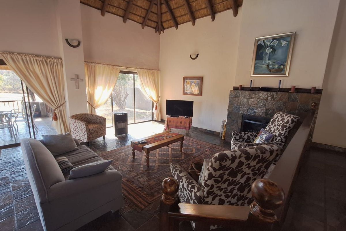 Spacious living room featuring a high thatched ceiling, slate tile flooring, and a prominent stone-clad fireplace, with direct access to an outdoor patio area.