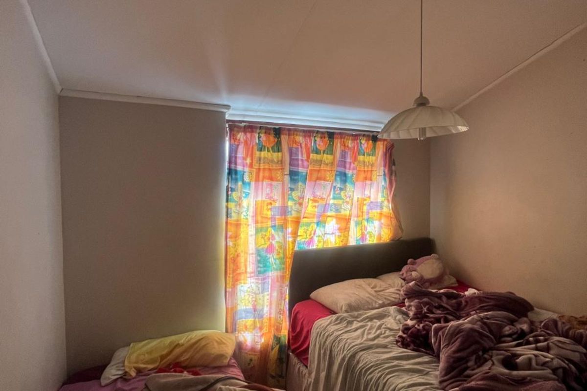 A compact bedroom featuring a window with natural light, neutral wall tones, and a central pendant light fixture.