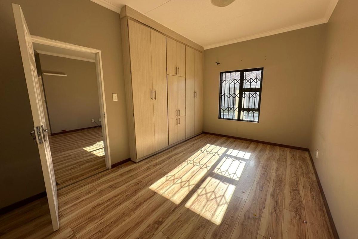A bright, empty bedroom featuring wood-look laminate flooring, built-in floor-to-ceiling cabinetry, and a window fitted with security bars.