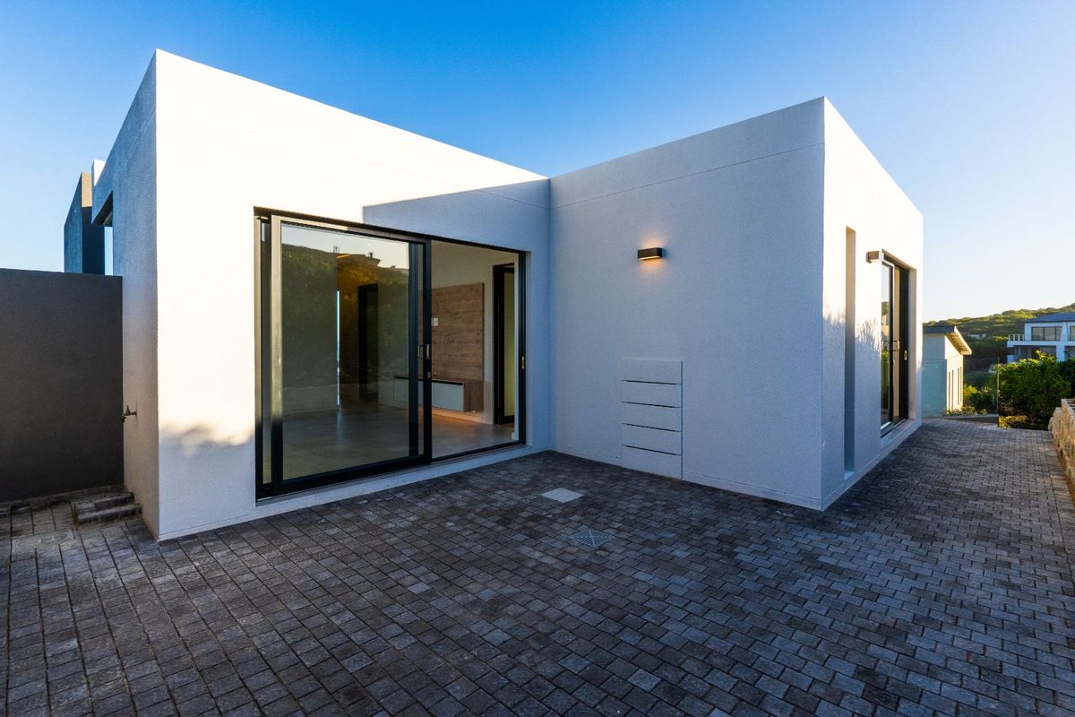 Modern exterior rear view featuring clean white rendered walls, large sliding glass doors, and a paved patio area.