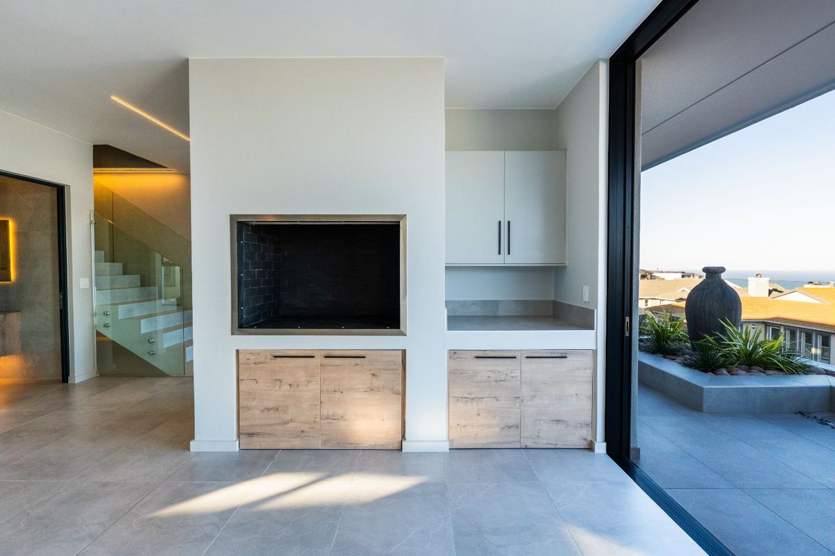 Modern indoor braai area featuring built-in cabinetry, stone countertops, and seamless access to an outdoor balcony with scenic views.