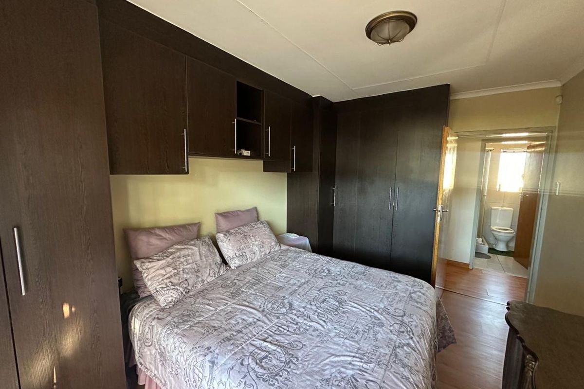 Bedroom featuring built-in dark wood cabinetry and laminate flooring, with an adjoining en-suite bathroom visible through the doorway.