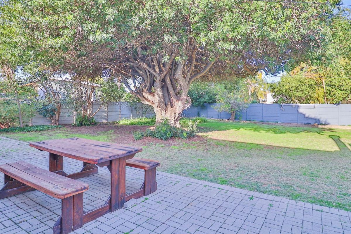 A spacious rear garden featuring a paved patio area, established mature tree, and perimeter boundary fencing.