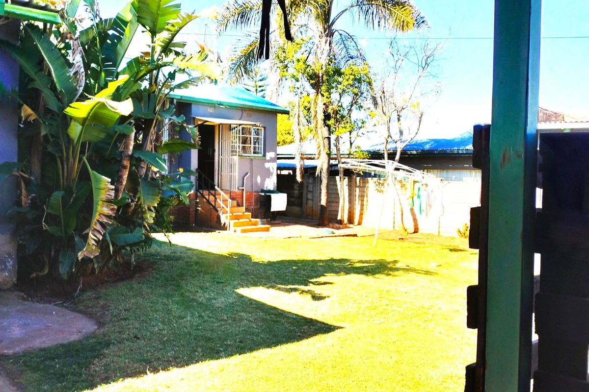 A view of the rear garden and backyard area, featuring a small outbuilding with stairs and a perimeter boundary wall.