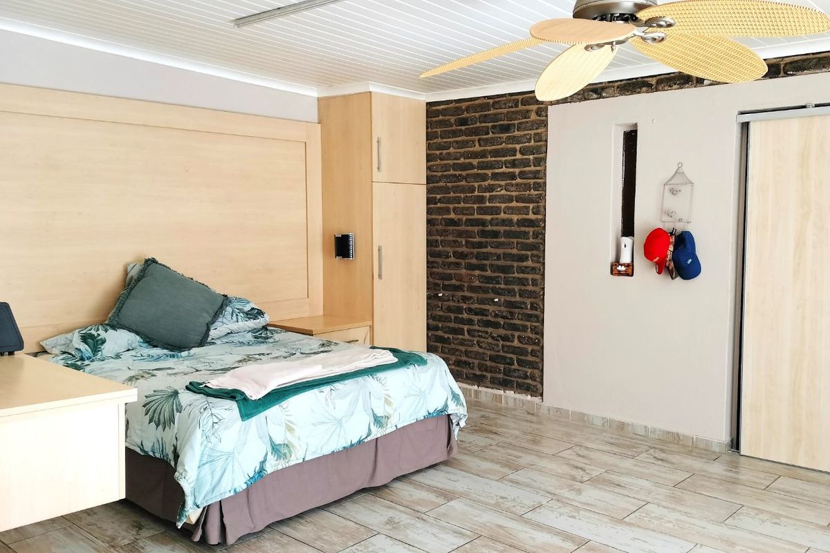 A bedroom featuring a built-in headboard and wardrobe unit, exposed brick feature wall, tiled flooring, and a ceiling fan.