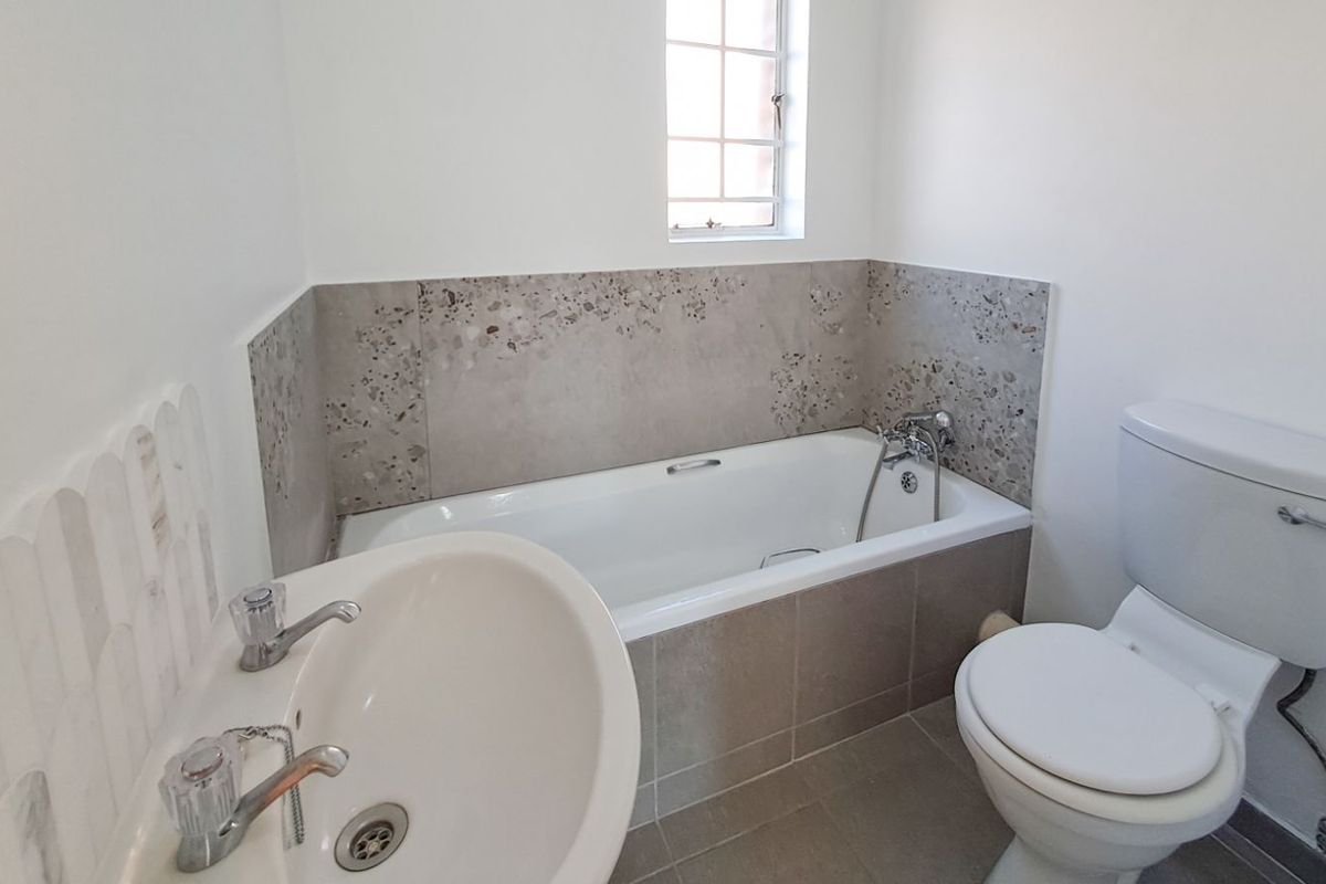 A clean, functional bathroom featuring a bathtub with a shower mixer, a pedestal basin, and a toilet, finished with neutral wall and floor tiling.