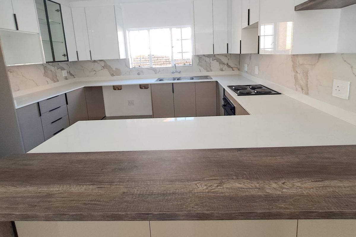 Modern kitchen featuring white cabinetry, stone countertops, marble-look splashbacks, and a breakfast bar with a wood-grain finish.