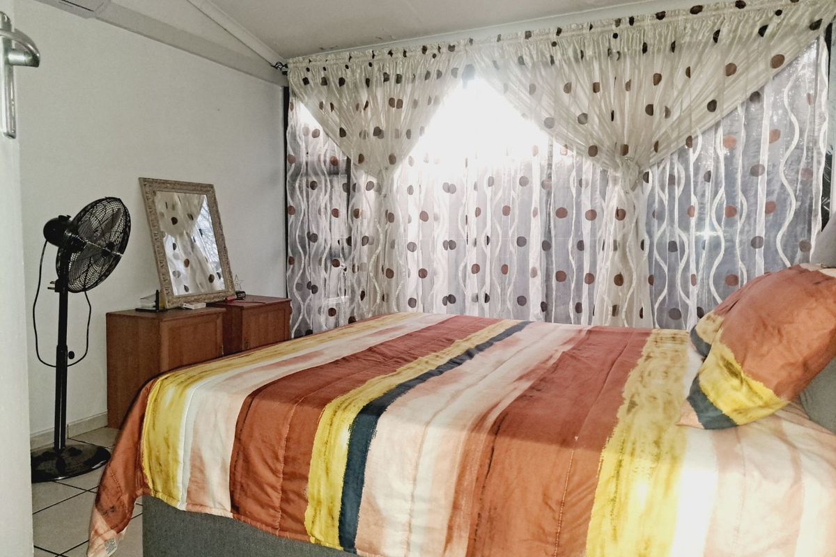 A bedroom featuring tiled flooring, a wall-mounted air conditioning unit, and large windows covered by curtains.