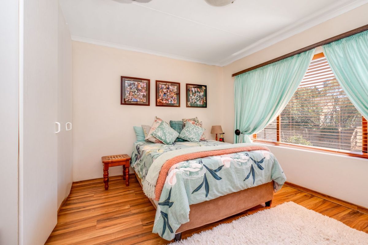 A well-maintained bedroom featuring built-in cupboards, warm wood-look flooring, and a large window allowing for natural light.