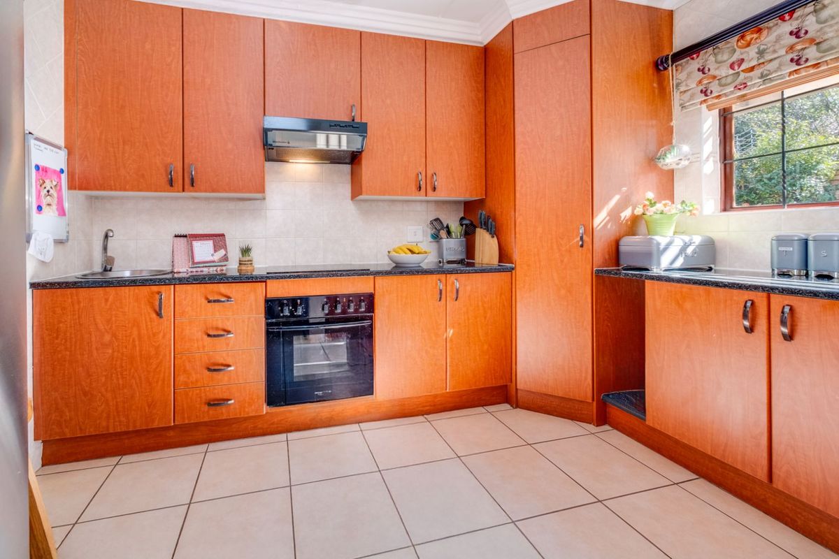 A functional kitchen featuring wood-finish cabinetry, dark granite countertops, a built-in oven, extractor fan, and tiled flooring.