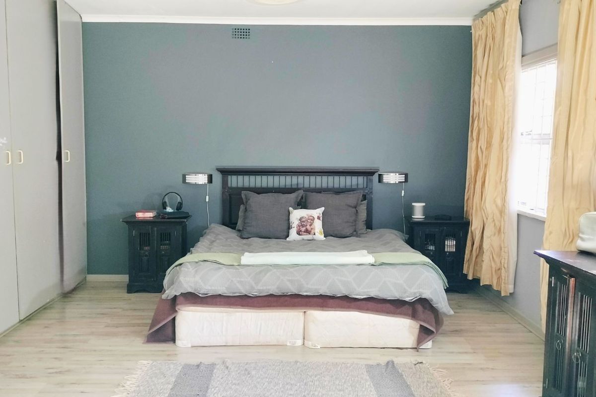A spacious bedroom featuring built-in floor-to-ceiling wardrobes, light-toned laminate flooring, and a feature wall.