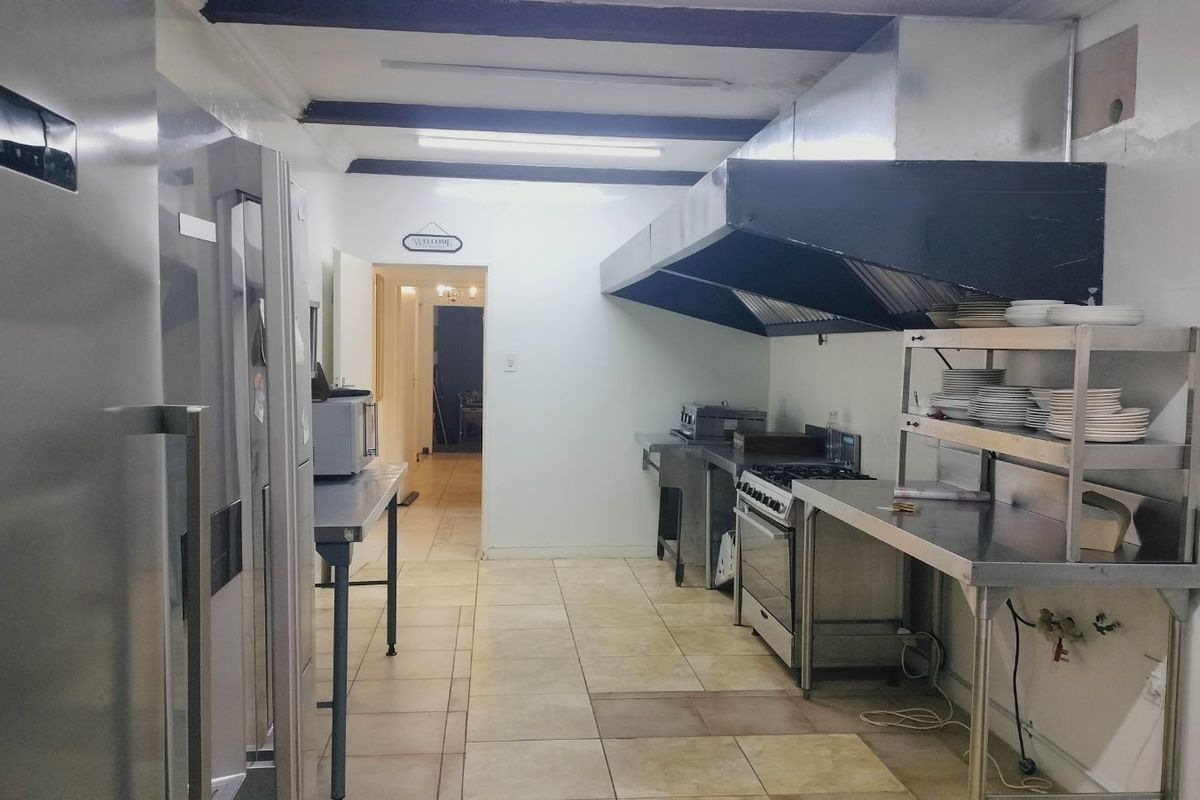 Commercial-style kitchen featuring stainless steel work surfaces, a large extractor hood, and tiled flooring, suitable for high-volume food preparation.
