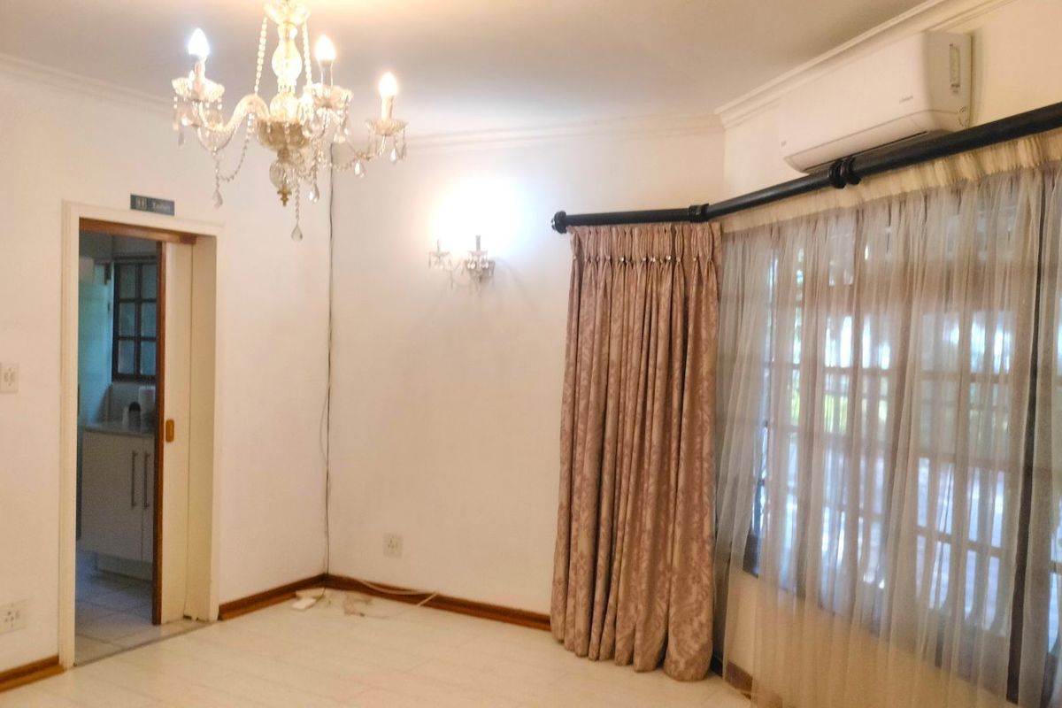 A living room featuring tiled flooring, a wall-mounted air conditioning unit, and a decorative chandelier, with an adjacent doorway leading to a kitchen area.