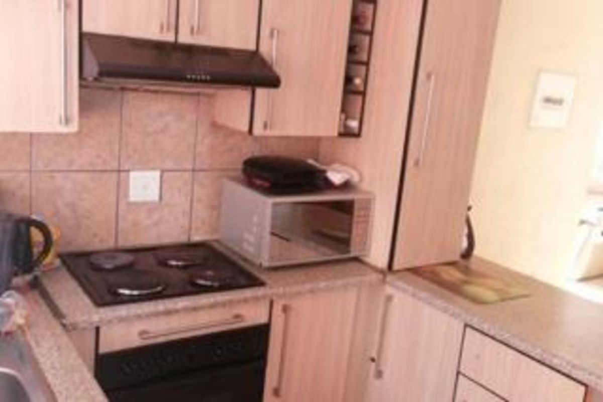 A compact kitchen featuring light wood-finish cabinetry, a built-in electric hob, an extractor fan, and a tiled backsplash.