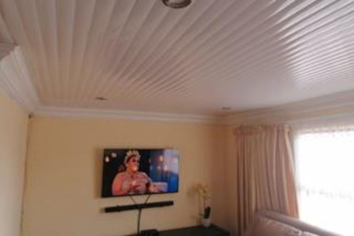 A living room featuring a distinctive tongue-and-groove style ceiling with recessed downlights and crown molding.