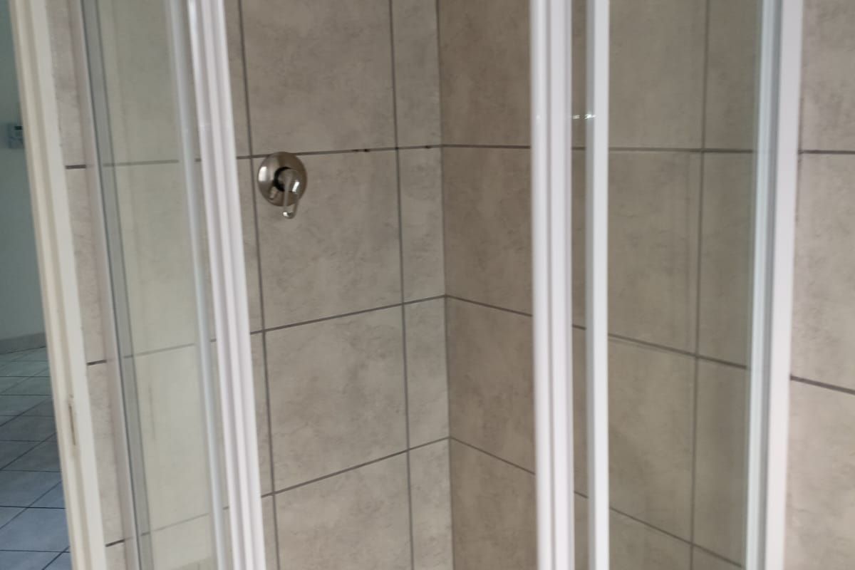 A clean, modern shower enclosure featuring neutral wall tiling, a white shower tray, and a chrome mixer tap with a fixed shower head.