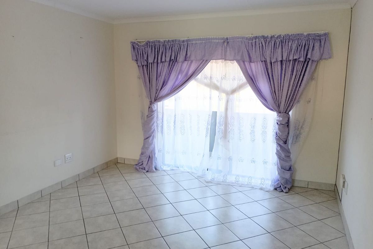 A bright, empty living room featuring neutral ceramic floor tiles and a large sliding glass door with curtain fixtures.