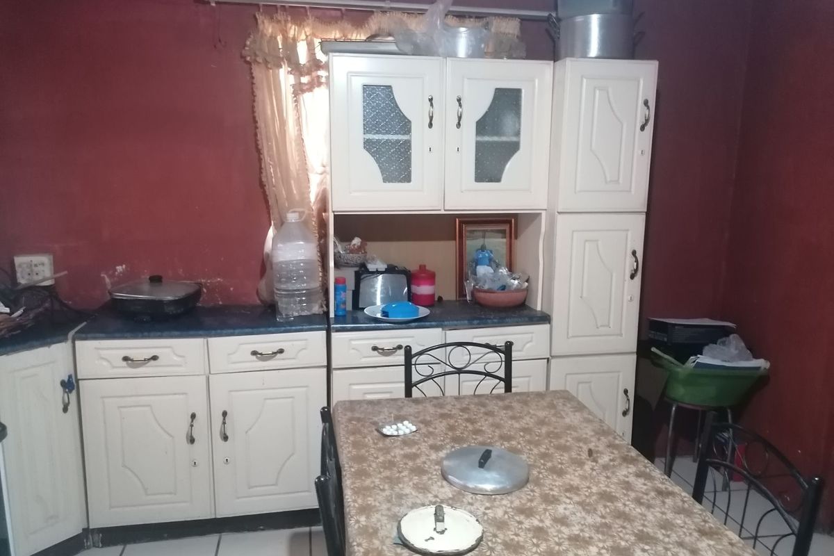 A dated kitchen area featuring traditional white cabinetry, tiled flooring, and dark red wall finishes, providing a functional but aged culinary space.