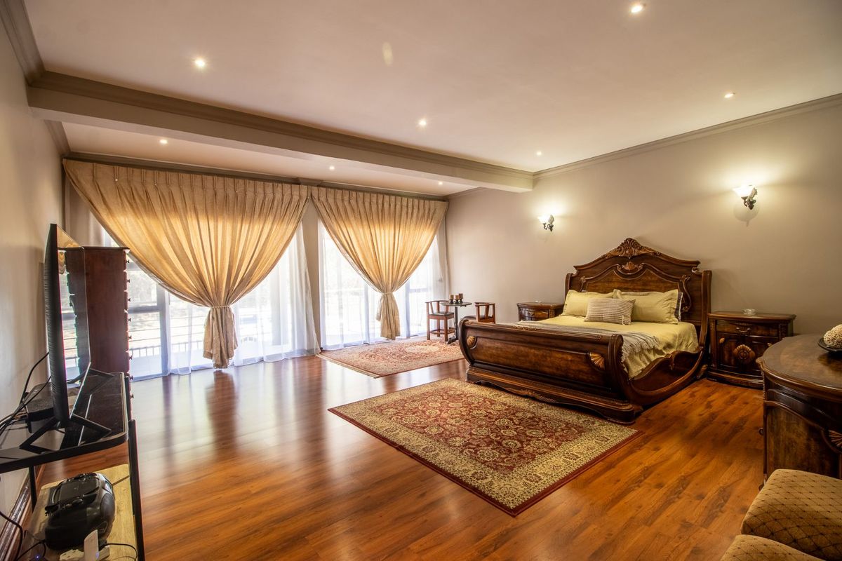 Spacious bedroom featuring polished timber flooring, recessed downlighting, and large sliding glass doors with floor-to-ceiling curtains providing ample natural light.