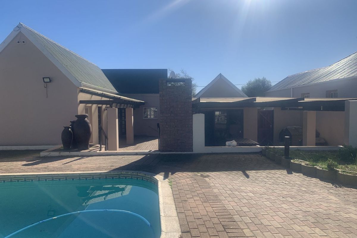 Rear exterior view featuring a swimming pool, paved patio area, and covered pergola structure attached to the main house.