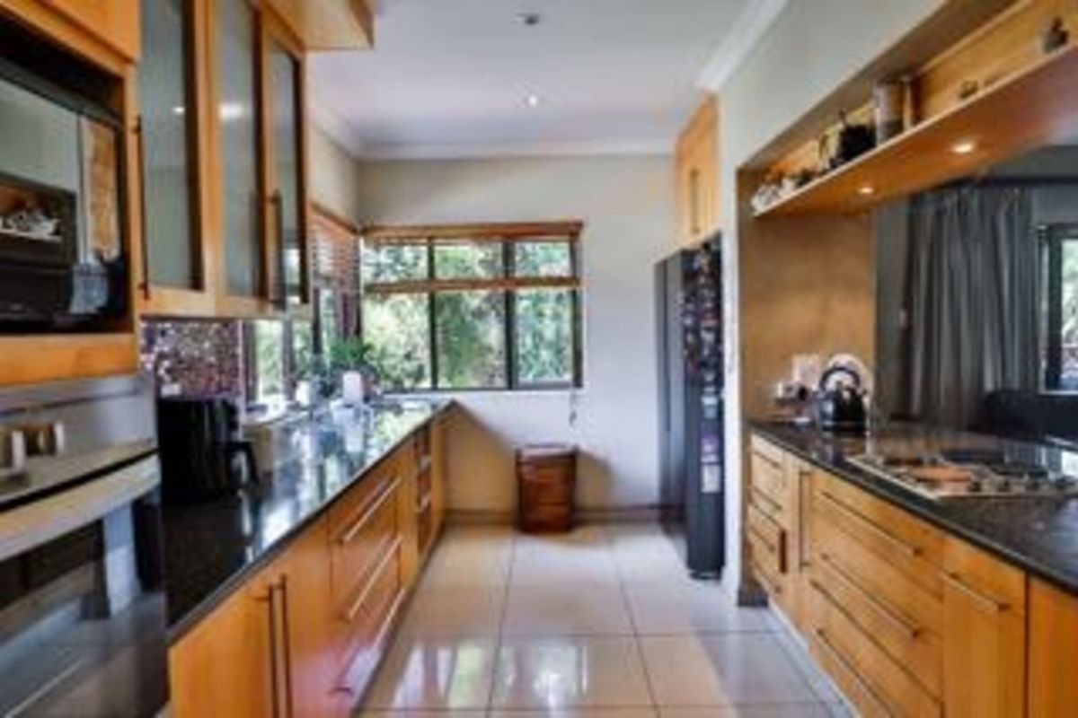 A functional galley-style kitchen featuring warm timber cabinetry, dark granite countertops, built-in oven, and a gas hob, complemented by tiled flooring and natural light.