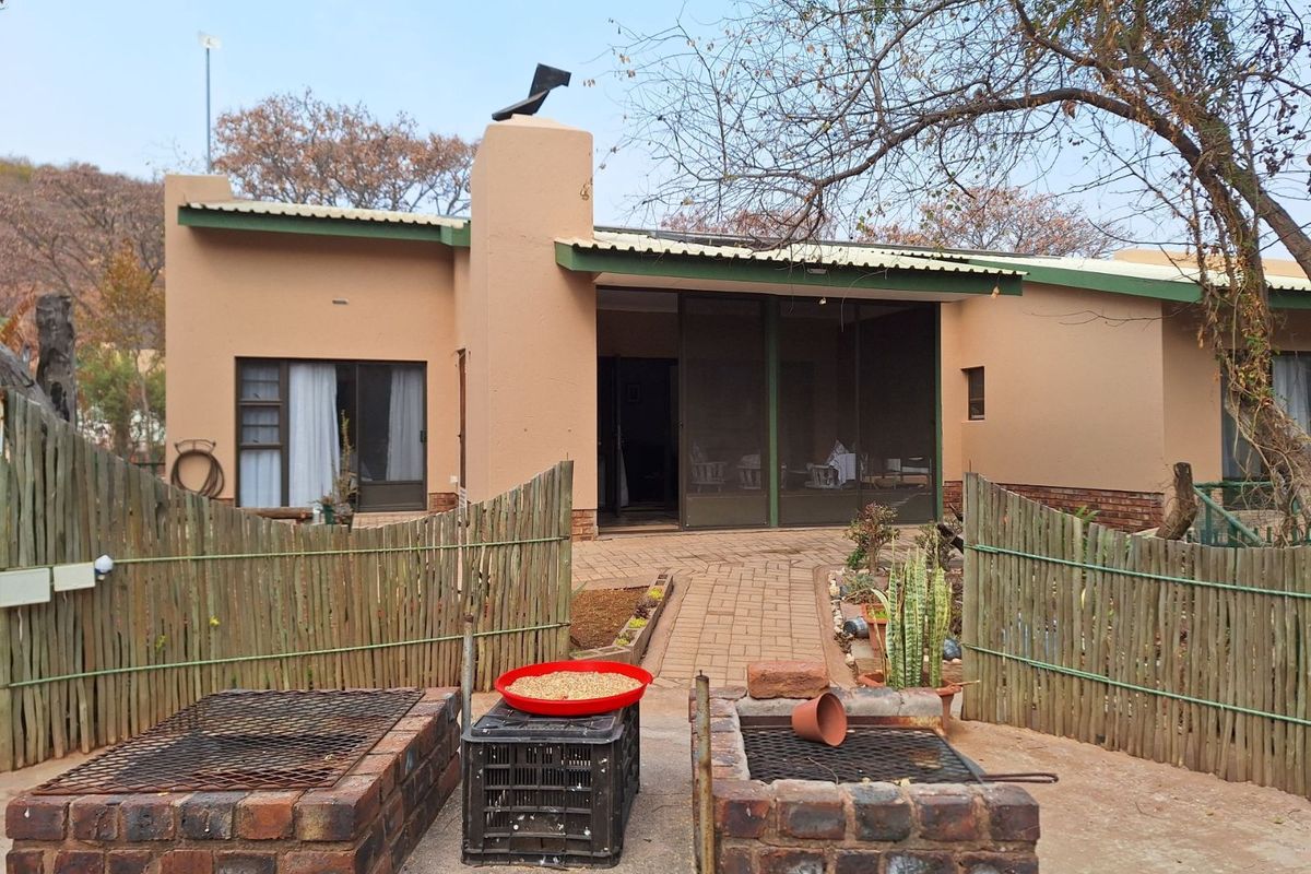 A rear exterior view of the house featuring a paved patio area, built-in brick braai facilities, and a screened-in porch entrance.