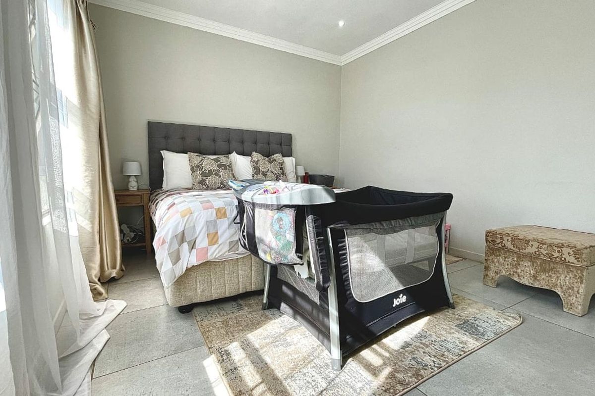 A well-maintained bedroom featuring neutral wall tones, crown molding, and large format floor tiles, providing a clean and functional living space.