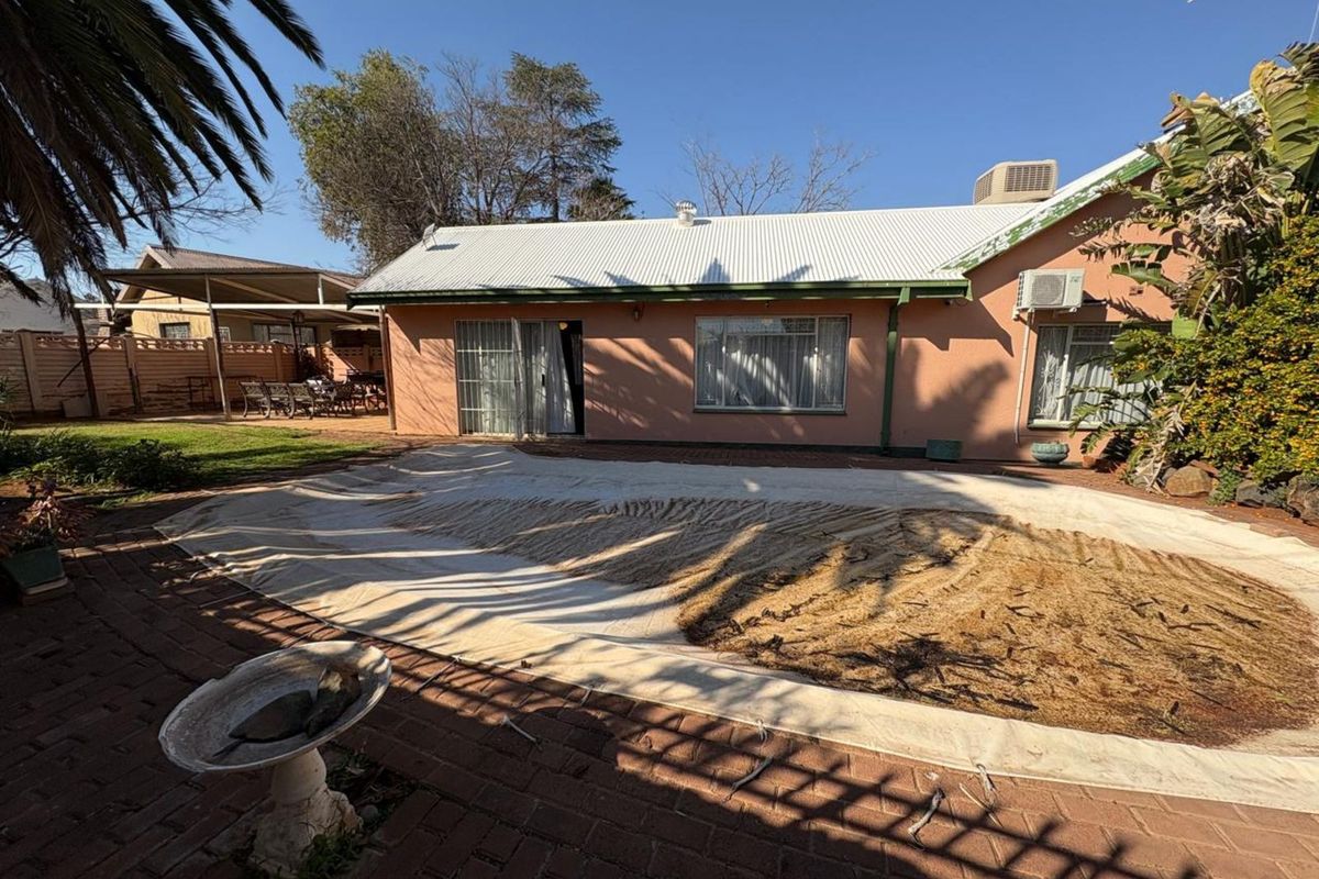 Rear view of the property featuring a swimming pool with a cover, paved patio area, and access to the main house structure.