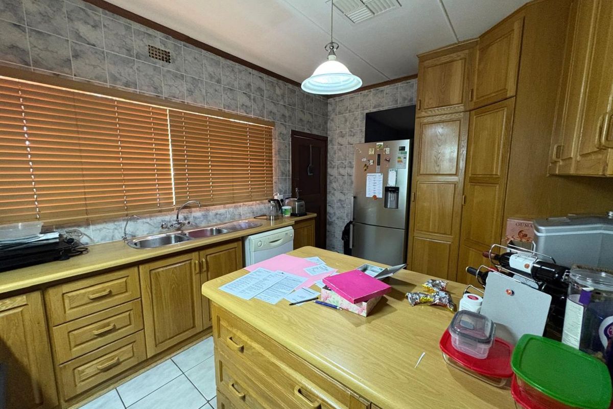A functional kitchen featuring timber cabinetry, a central island, double stainless steel sink, and tiled splashbacks.