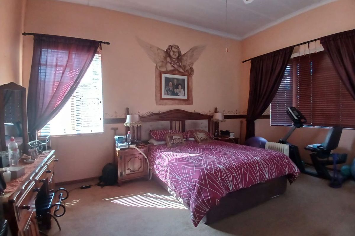 Spacious bedroom featuring large windows with blinds, ceiling fan, and carpeted flooring, offering a comfortable and functional living space.