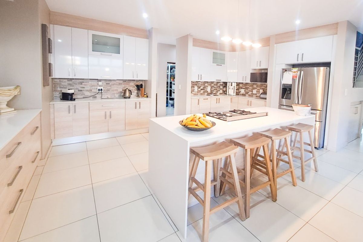 Modern open-plan kitchen featuring a central island with a built-in cooktop, sleek cabinetry, stone countertops, and tiled flooring.