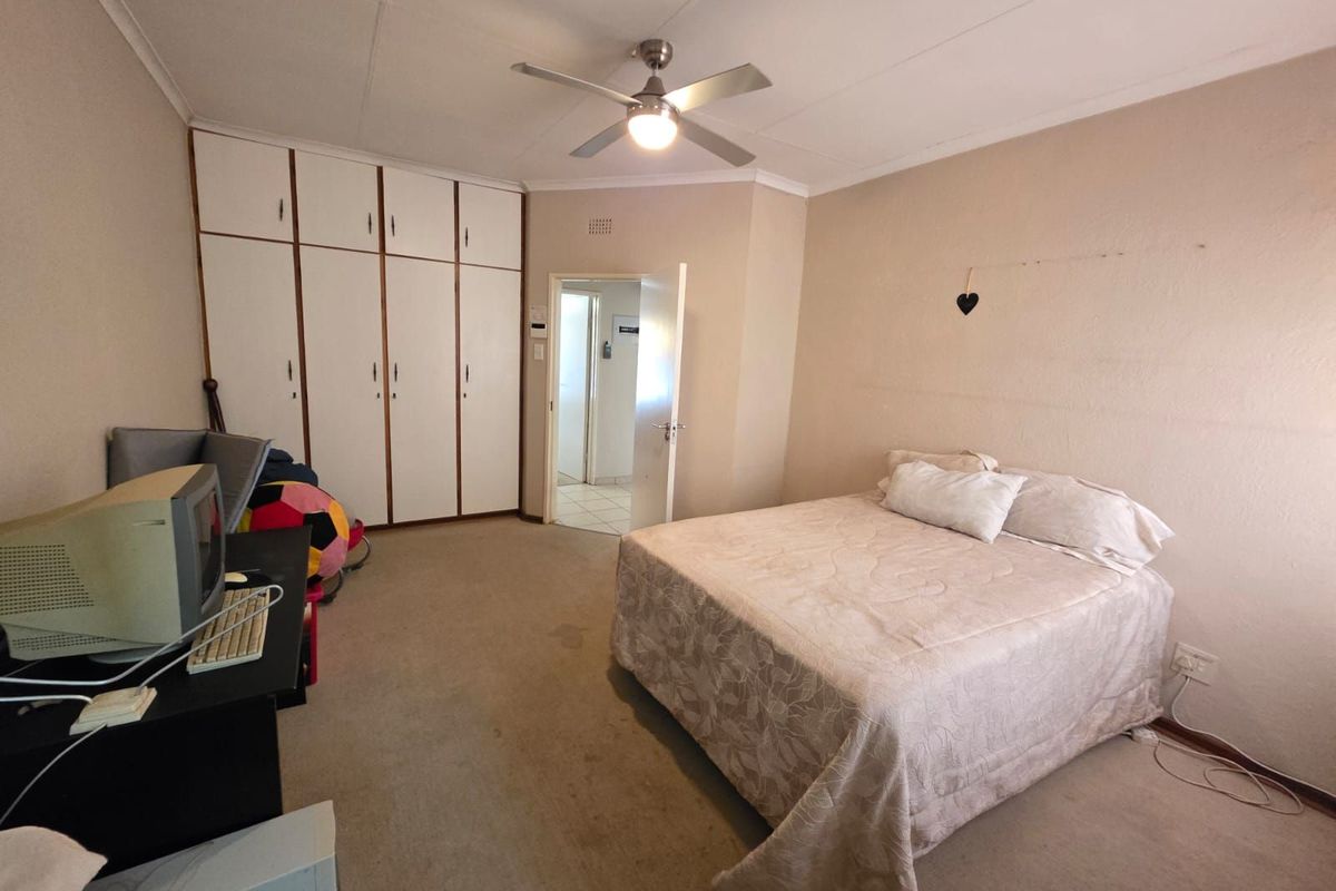 A spacious bedroom featuring built-in cupboards, a ceiling fan, and direct access to an adjoining room.