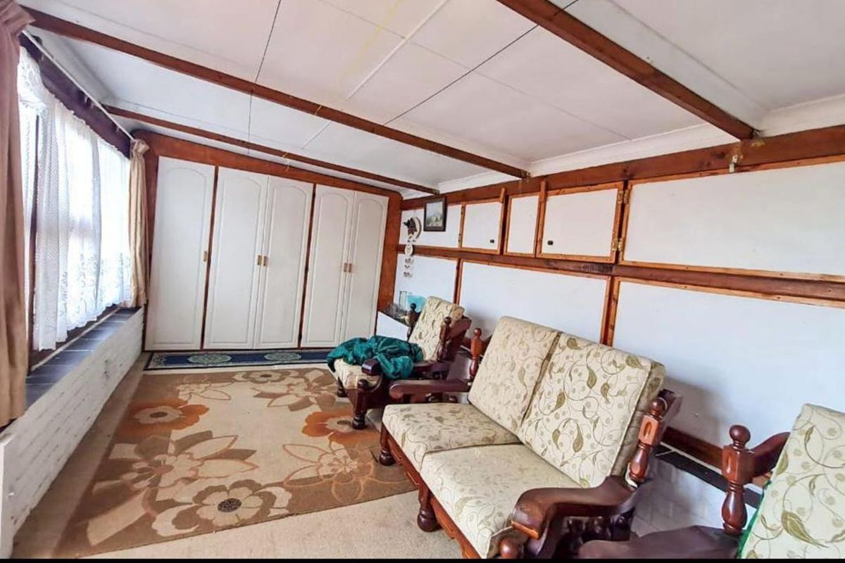 A sunroom or living area featuring built-in cabinetry, timber ceiling beams, and wall paneling, offering a dated aesthetic with potential for modernization.