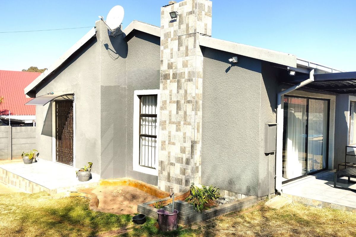 Rear view of the property featuring a stone-clad chimney, covered patio area with sliding doors, and a low-maintenance garden space.