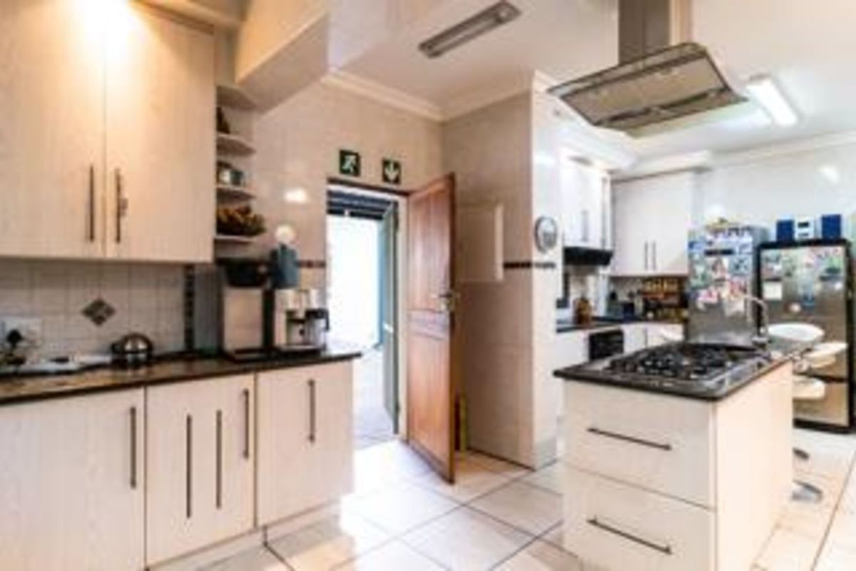 A functional commercial kitchen featuring light-toned cabinetry, a central island with a gas hob, stainless steel extractor fan, and tiled flooring.