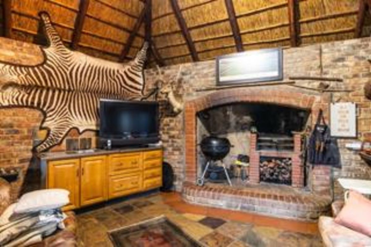 Rustic entertainment area featuring a large built-in brick fireplace, exposed thatch roof, and tiled flooring, creating a traditional lodge-style atmosphere.