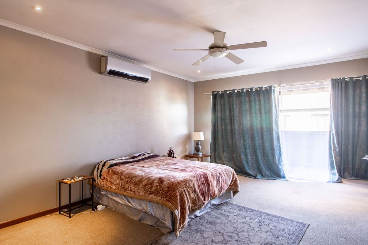 A spacious bedroom featuring a wall-mounted air conditioning unit, ceiling fan, and large sliding glass doors leading to an outdoor area.